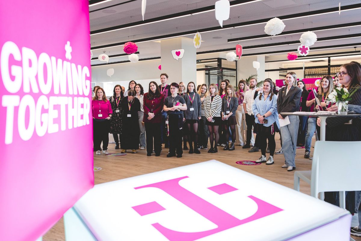 A group of people attending an indoor event with a pink theme, featuring a "Growing Together" sign and decorative hanging elements.