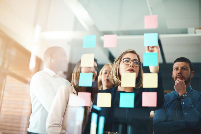 A group of people in an office setting brainstorm using colorful sticky notes on a glass wall.