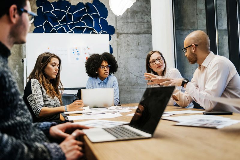 Group of diverse people discussing while sitting together in a meeting room with papers and laptops on the table.
