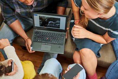 A group of people sitting on a couch, looking at a laptop displaying a black and white photo. One person holds a smartphone.