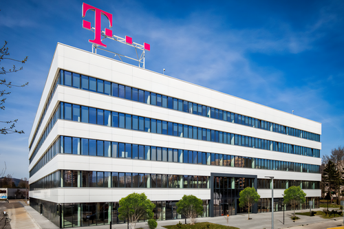 Modern, multi-story office building with large windows, a red "T" logo on the roof, and a clear blue sky in the background.
