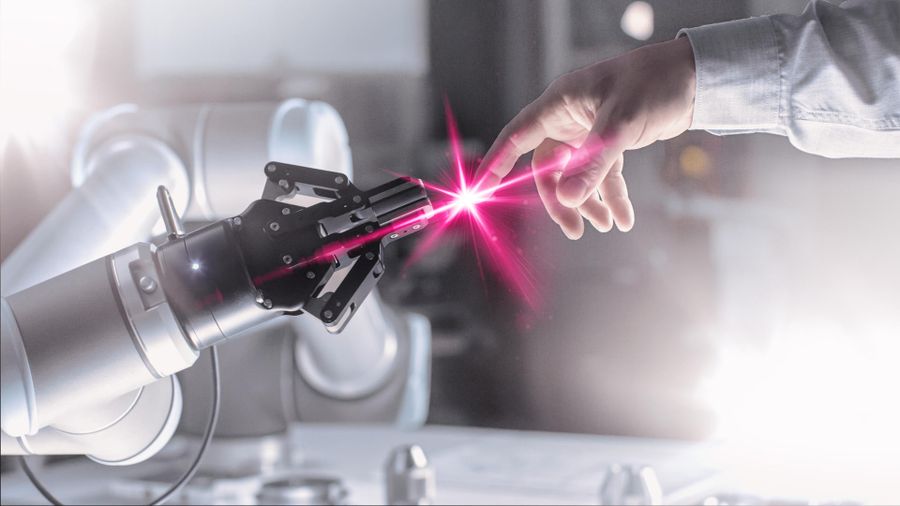 A human hand touches a robotic hand, creating a bright pink spark at the fingertips, symbolizing human-robot interaction.