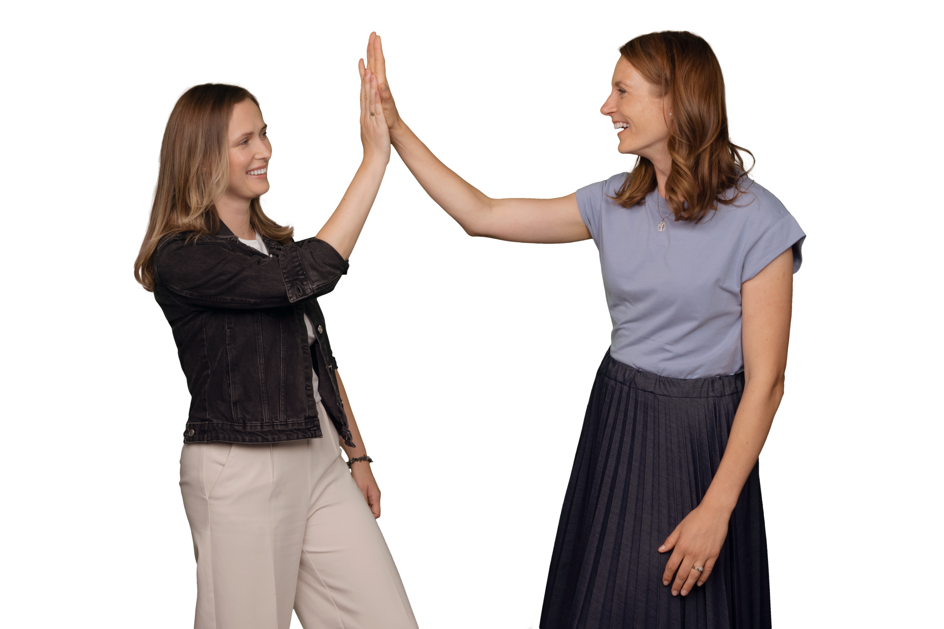 Two women smiling and giving each other a high-five, one wearing a denim jacket, the other in a blue top.