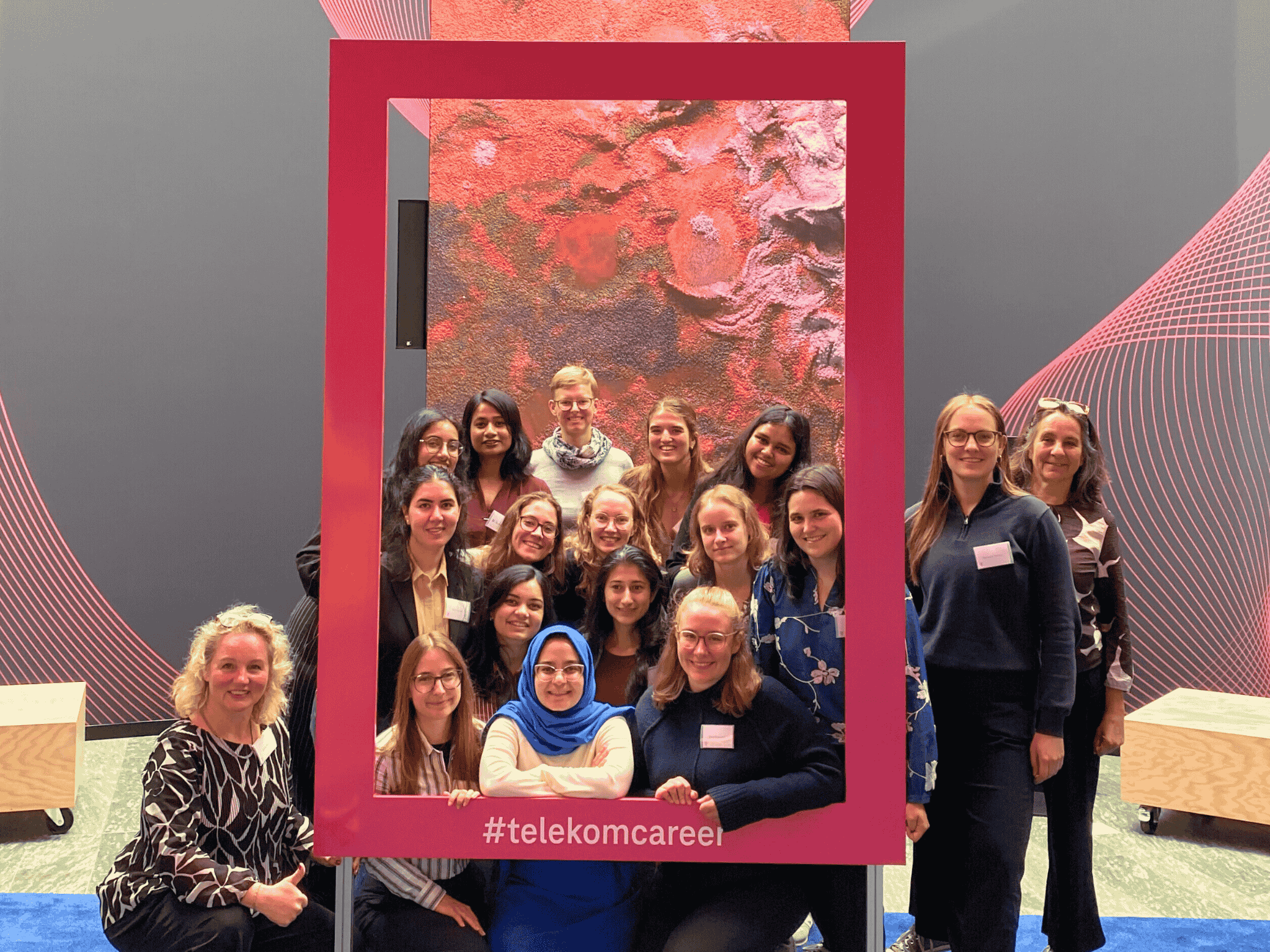 A group of people smiling, posing within a large pink frame labeled "#telekomcareer" against a colorful abstract background.