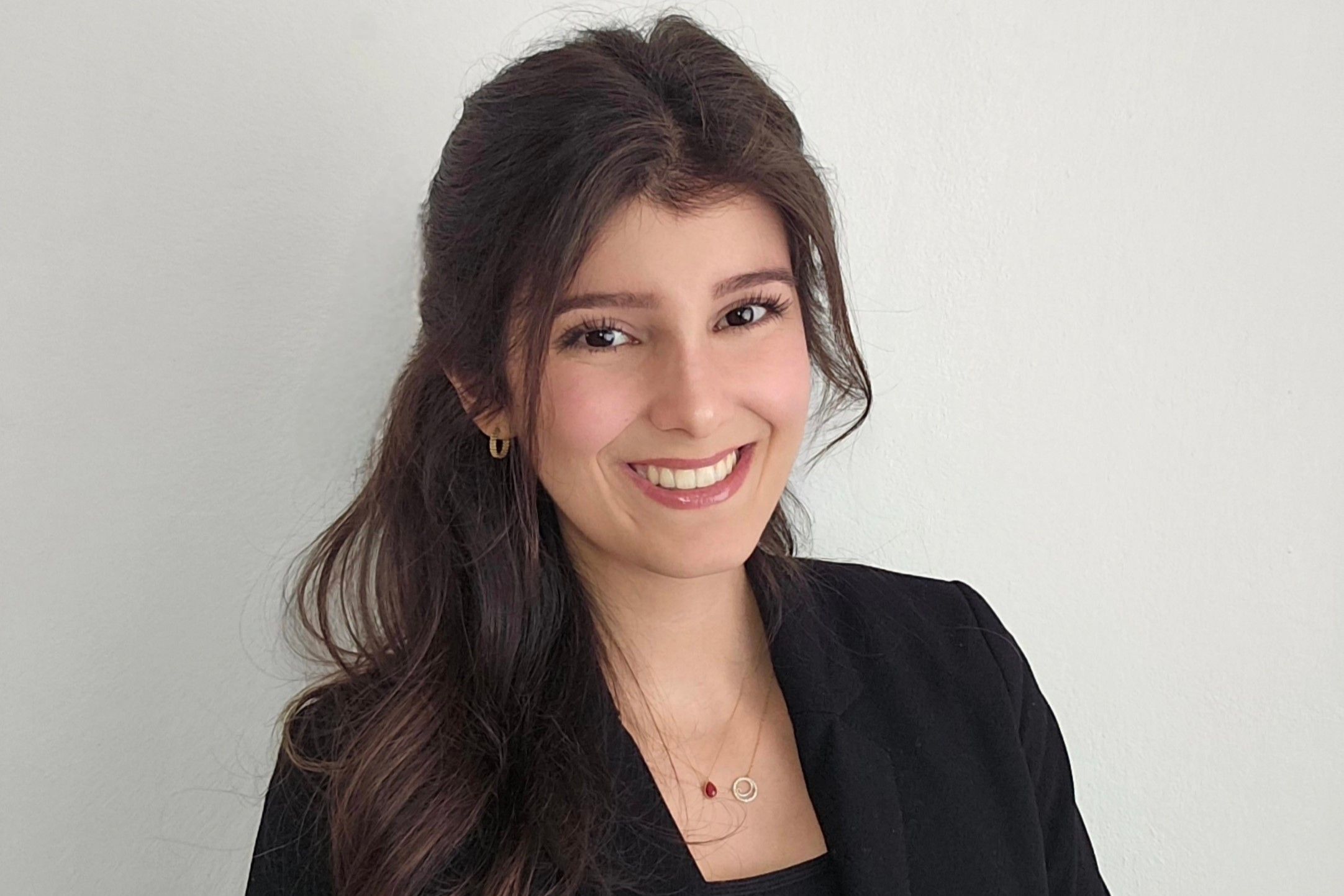 Smiling woman with long dark hair, wearing a dark blazer, against a gray background.