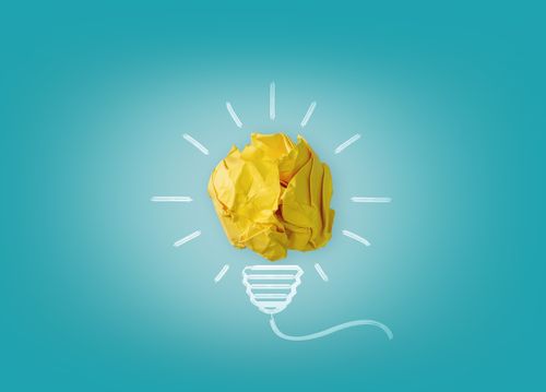 Crumpled yellow paper forms a light bulb shape with drawn lines on a blue background, symbolizing creativity and ideas.
