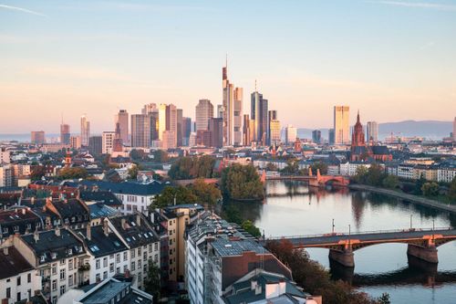 Aerial view of Frankfurt skyline at sunset, featuring modern skyscrapers, traditional buildings, and a river with bridges.