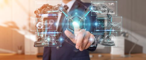 Person in a suit interacting with a virtual interface displaying robotic arms and digital graphics in a modern office setting.