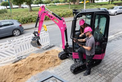 Magenta Bagger mit zwei Kolleg*innen an einer Baustelle