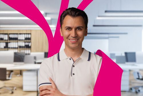 Smiling man in a white polo shirt stands with arms crossed in a modern office, with magenta abstract shapes in the foreground.