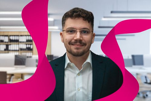 Smiling man in glasses and suit stands in a modern office, with magenta abstract shapes in the foreground.