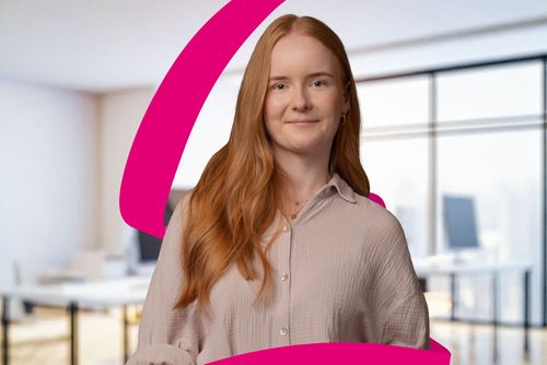 A person with long red hair smiles, standing in a bright office. A pink graphic element is overlaid on the image.