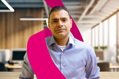 Man in a light blue shirt stands in a modern office, with a magenta ribbon design in the foreground.