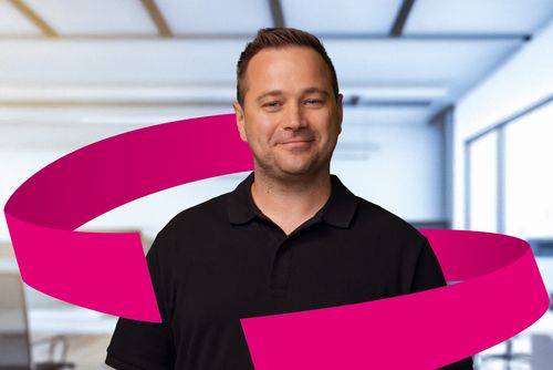 Man in a black polo shirt standing in a modern office with a magenta ribbon graphic around him.