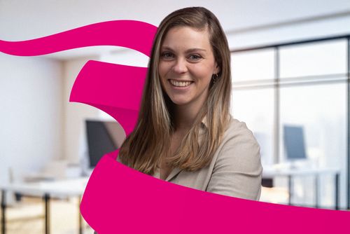 Smiling woman in a beige shirt with long hair stands in an office, partially framed by a magenta ribbon graphic.