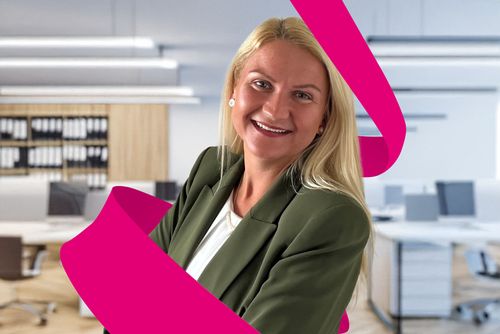 Smiling woman in a green blazer stands in a modern office, with a pink ribbon graphic in the foreground.