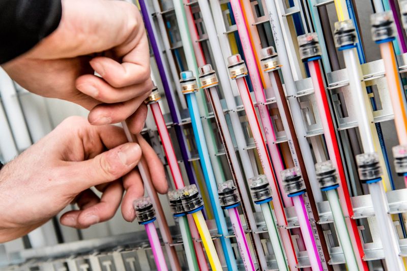 Hands adjusting colorful cables in a network or server rack, showcasing a variety of vibrant wires and connectors.