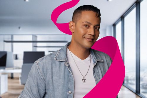 Smiling person in a denim jacket and white shirt, standing in a modern office with large windows and a pink ribbon graphic.