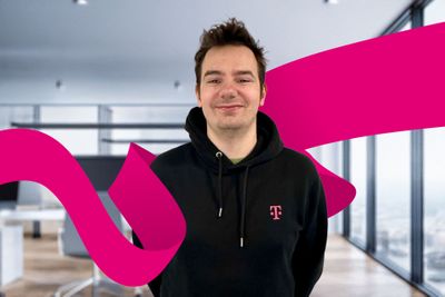 Smiling person in a black hoodie stands in a modern office, with a magenta ribbon design in the background.