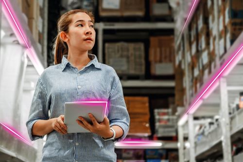 A woman in a warehouse holds a tablet, surrounded by shelves filled with boxes. Neon pink lines add a futuristic touch to the scene.
