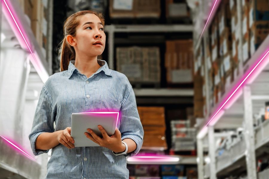 A woman in a warehouse holds a tablet, surrounded by shelves filled with boxes. Neon pink lines add a futuristic touch to the scene.