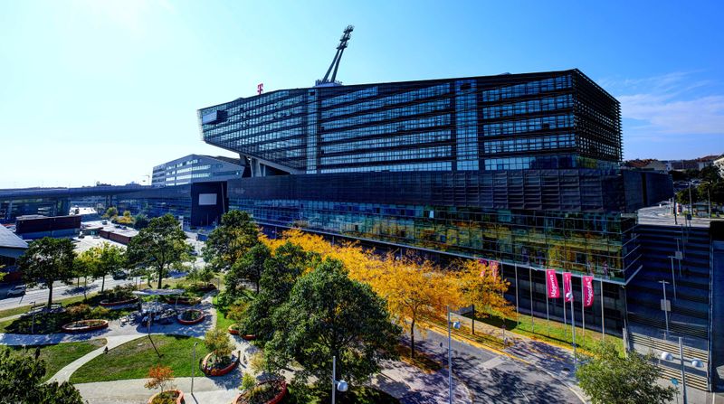 Modern building with glass facade and unique architecture, surrounded by trees and a landscaped park under a clear blue sky.