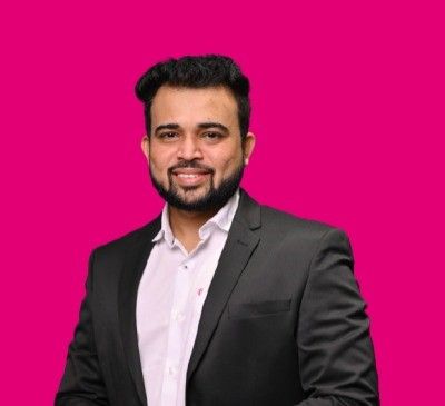 Smiling man in a black suit and white shirt against a bright magenta background.