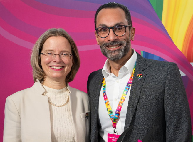 Two people smiling in front of a colorful background.