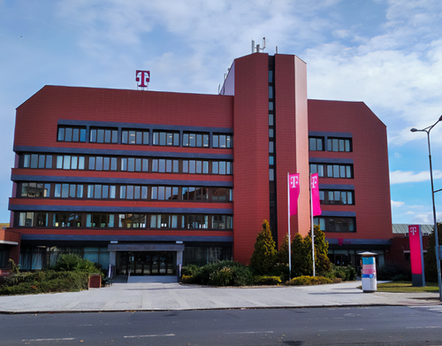 A modern red-brick office building with a telecommunications logo, featuring large windows and pink flags, under a partly cloudy sky.