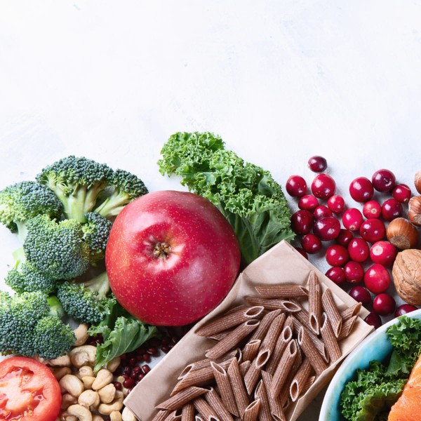 Exemples d'aliments riches en fibres sur une table, avec une pomme, des pâtes complètes, des brocolis et des noix de cajou