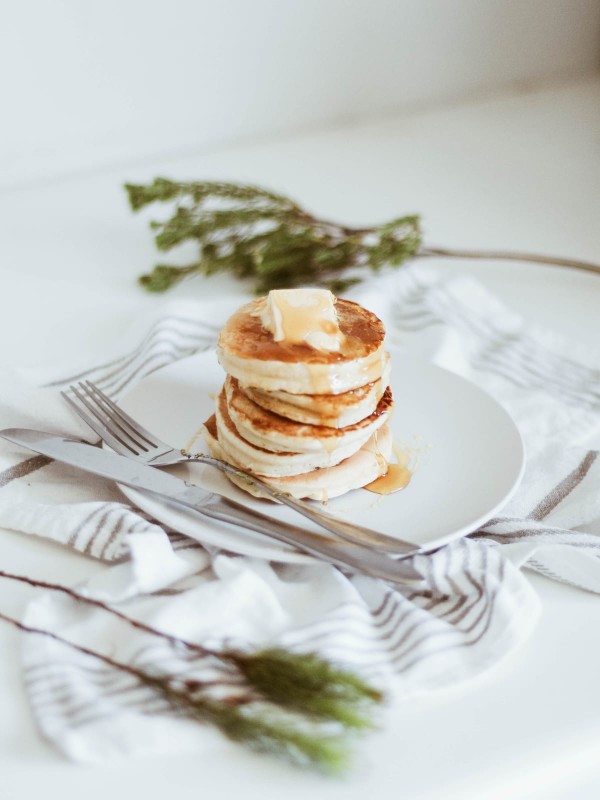 Pile de pancakes dans une assiette avec un filet de sirop d'érable, un sucre non raffiné