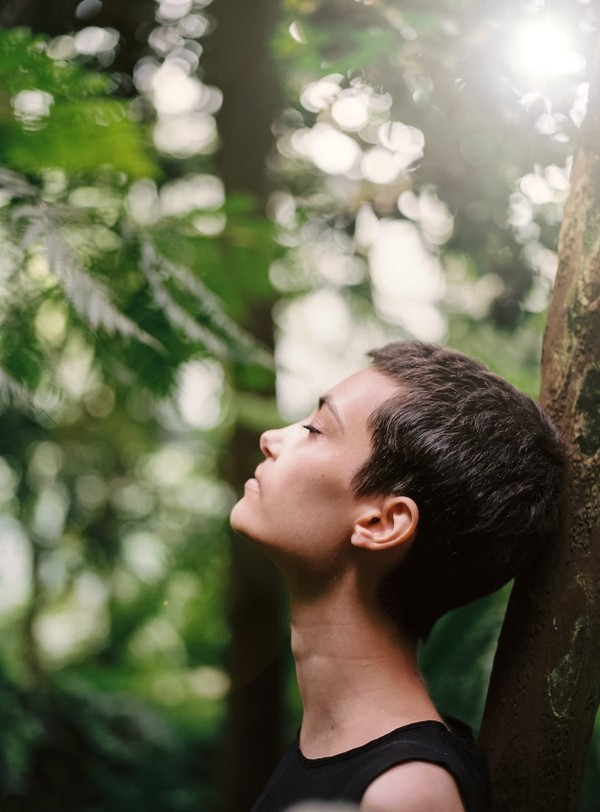 Jeune femme en train de méditer en pleine nature, adossée à un arbre