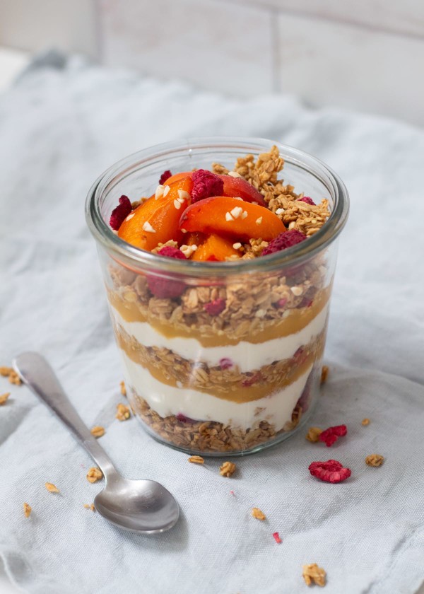 Layer jar avec yaourt végétal, granola et morceaux d'abricots sur une table avec une cuillère