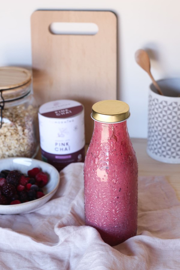 Bouteille de smoothie fruits rouges avec un bol de fruits rouges et un bocal de flocons d'avoine en arrière plan