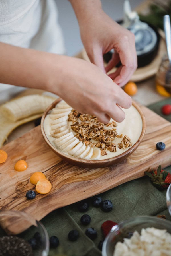 Femme préparant un bol de granola avec une banane et des myrtilles pour son petit-déjeuner