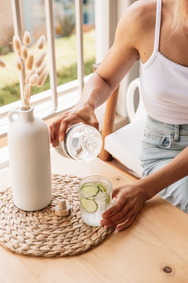Jeune femme se servant un verre d'eau sur une table, pour sa routine matinale