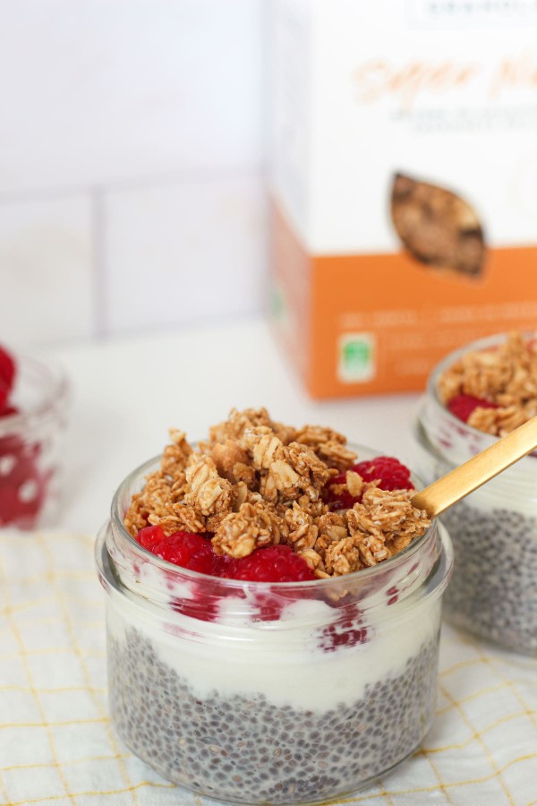 Pudding de chia avec framboises, granola et beurre de cacahuète en topping, à côté d'un paquet de granola