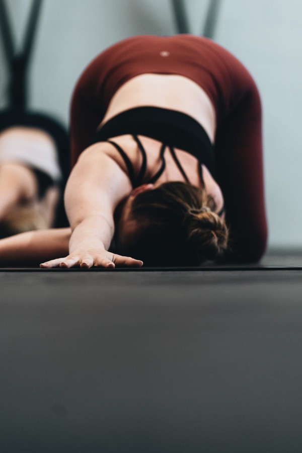 Jeune femme en tenue de yoga sur son tapis, dans une posture d'étirement pour lâcher prise et s'assouplir