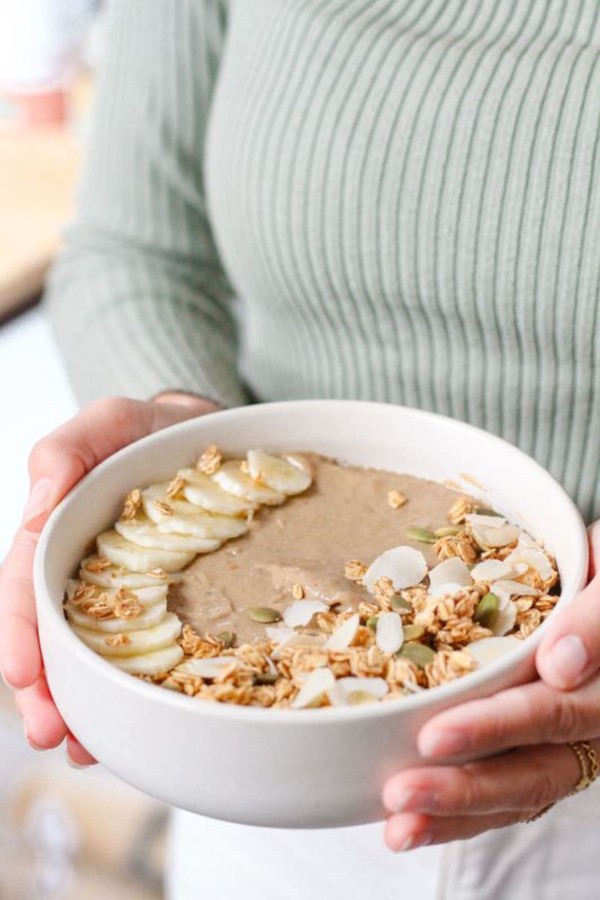 Bol de granola enrichi en probiotiques, à la banane, aux copeaux de noix e coco et aux graines de tournesol, tenu en main par une femme