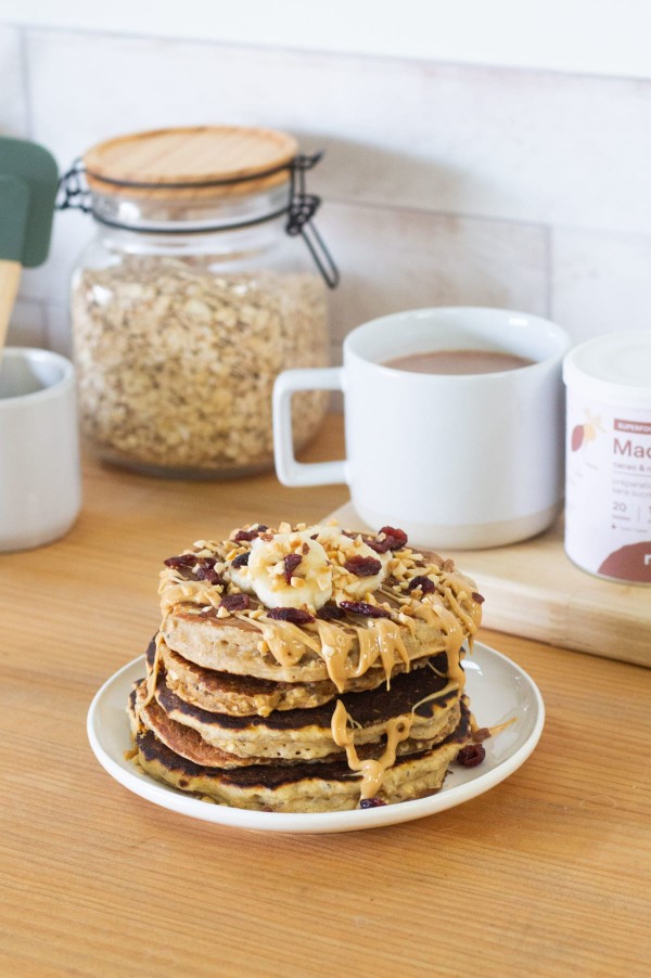 Pile de pancakes garnis de coulis de chocolat, beurre de cacahuète, tranches de banane et granola dans une assiette