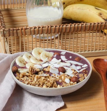 Açaï bowl avec toppings de banane et copeaux de noix de coco, servi sur une table avec une banane et un verre de lait végétal