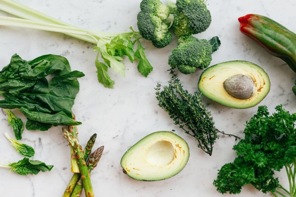 Aliments anti fatigue sur une table, comme un avocat coupé en deux, du brocoli, trois brins d'asperge, des feuilles d'épinard et du persil