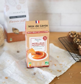 Un paquet de préparation pour muffins à la noisette sur une table, avec des muffins sur une plaque de cuisson et un paquet de granola en arrière plan