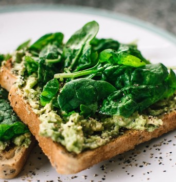 Deux tartines de pain grillé avec des aliments anti fatigue comme l'avocat et des épinards dans une assiette