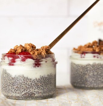 Deux puddings de chia avec de la framboise, du granola et du beurre de cacahuète en topping, sur une table de petit-déjeuner