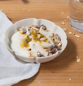 Bol de muesli maison avec yaourt végétal, copeaux de coco et morceaux de dattes séchées sur une table de petit-déjeuner