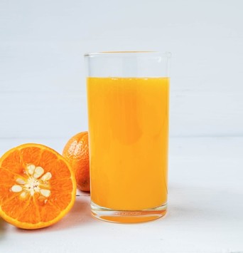 Un grand verre de jus d'orange pour le matin, à côté d'une orange coupée en deux