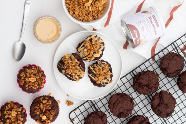 Muffins végans au chocolat avec un filet de beurre de noix et du granola en topping, sur une table de petit-déjeuner