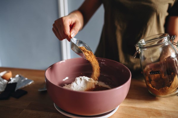 Une femme prépare un gateau et verse du sucre de coco dans un saladier avec de la farine