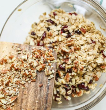 Bol de granola maison avec des noix et des cranberries, et une planche à découper avec des flocons d'avoine